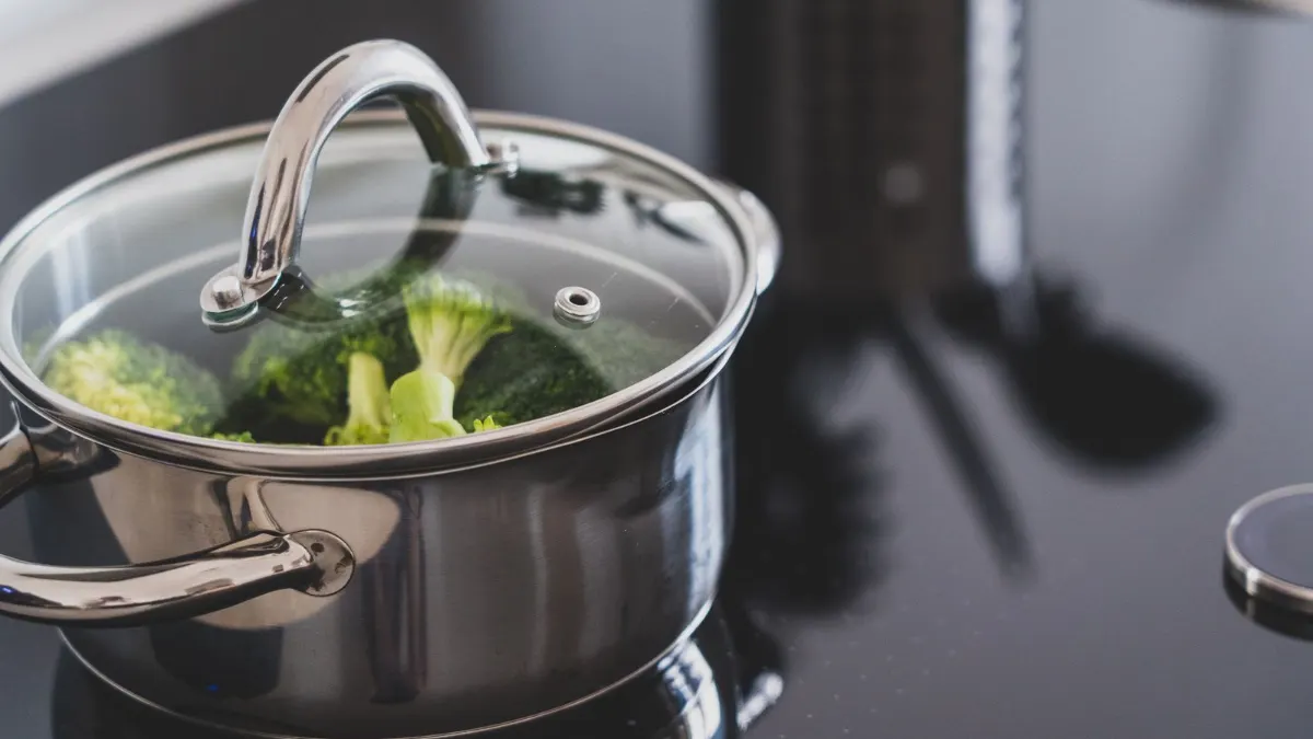 Olla de acero inoxidable con brócoli sobre una placa negra