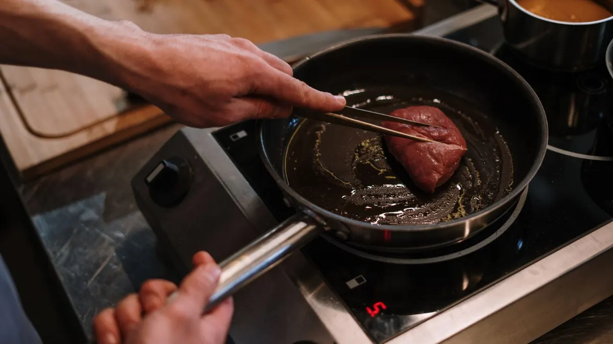 Mano dorando carne en una sartén sobre una placa de inducción